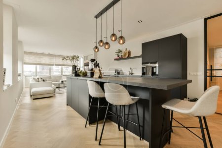 Foto de Una cocina y comedor en un apartamento moderno con paredes blancas, pisos de madera y armarios negros en la isla - Imagen libre de derechos