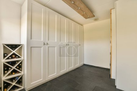 Photo for A wine rack in the corner of a room with white cupboards and shelves on the wall is made out of wood - Royalty Free Image