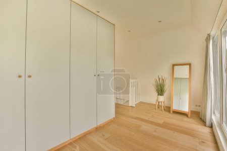 Photo for An empty room with white cupboards and a plant in the corner on the right hand side of the room - Royalty Free Image