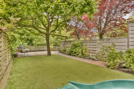Téléchargez les photos : Une arrière-cour avec herbe verte, des arbres et des clôtures en bois en arrière-plan est une petite piscine entourée d'un feuillage luxuriant - en image libre de droit