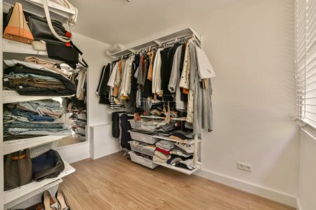Photo for A walk - in closet with lots of clothes hanging on the walls and wooden flooring, all neatly organized - Royalty Free Image