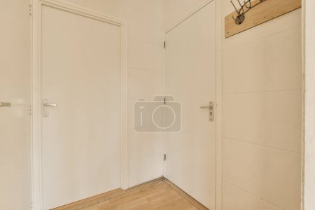 Photo for An empty room with white doors and wood flooring on the right side of the room, there is a clock above the door - Royalty Free Image