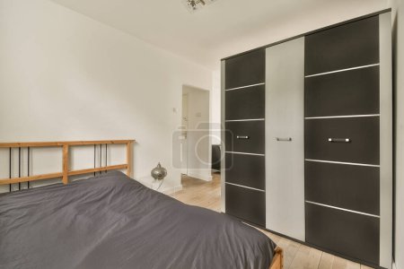 Photo for A bedroom with black and white closets on the wall next to the bed in the room has wood flooring - Royalty Free Image