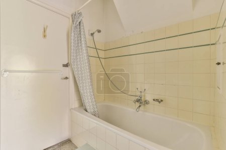 Photo for A bathroom with a bathtub, shower curtain and toilet paper on the wall next to the tub is white - Royalty Free Image