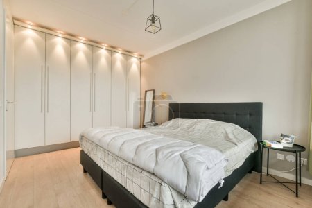 Photo for A bedroom with a bed and closets on the wall behind it in this photo, there is a lamp above the bed - Royalty Free Image