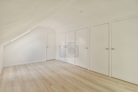 Photo for An empty room with white walls and wood flooring on the right side of the room, there are three closed doors - Royalty Free Image