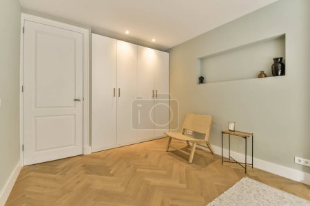 Photo for A room with wood flooring and white closets on the right side, there is a wooden chair in front of the door - Royalty Free Image