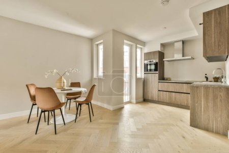 Photo pour Une cuisine et une salle à manger dans une maison avec parquet, murs blancs et armoires en bois clair de chaque côté - image libre de droit
