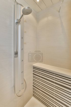 Téléchargez les photos : A bathroom with white tiles on the walls and shower head mounted to the wall in front of the bathtub - en image libre de droit