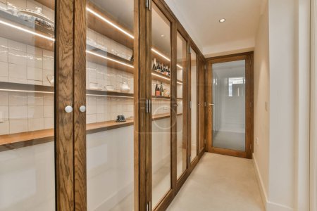 Photo for A long narrow hallway with wooden cabinets and white tiles on the walls, along with glass doors leading to another room - Royalty Free Image