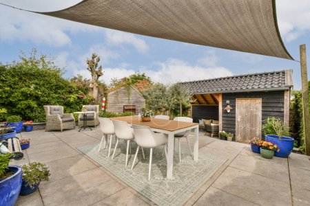 Photo for A patio area with chairs, tables and an umbrella over the dining table in front of a wooden shed behind - Royalty Free Image