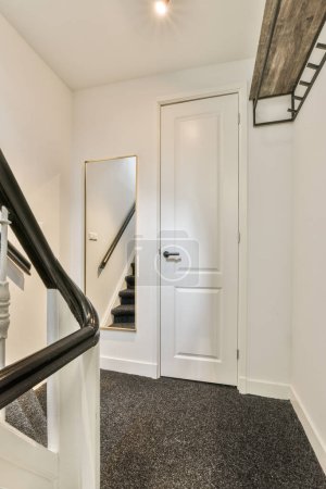 Foto de Una escalera blanca con alfombras negras y una puerta abierta que conduce al segundo piso en un espejo está en la pared - Imagen libre de derechos