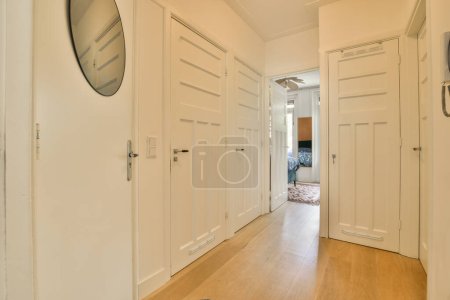 Photo for A long hallway with white doors and wood flooring on either side by side, looking into the living room - Royalty Free Image