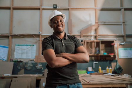Foto de Hombre africano feliz aprendiz carpintero supervisor confiado usando su sombrero duro en el trabajo en la fábrica. Foto de alta calidad - Imagen libre de derechos