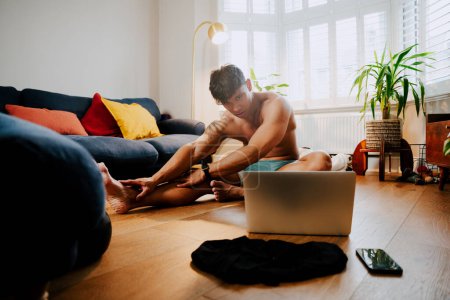 Photo for Asian young male working out with laptop at home in his lounge - Royalty Free Image