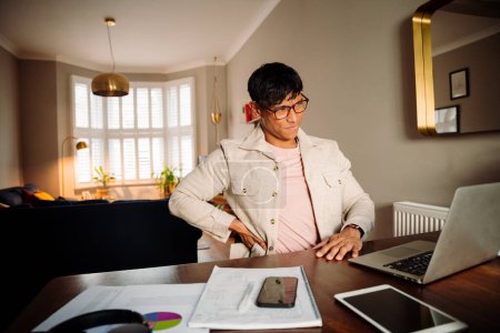 Photo for Asian man sitting at his desk working from his apartment on his laptop - Royalty Free Image