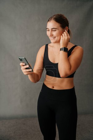 Photo for Close up young woman on her cellphone chatting before work out and using her ear pods. High quality photo - Royalty Free Image