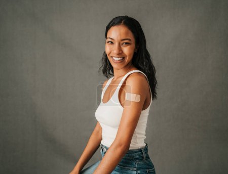 Photo for Close up Multiethnic female sitting smiling in her jeans with a band aid on her arm. High quality photo - Royalty Free Image