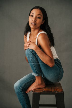 Photo for Multiethnic female sitting on high chair contemplating with her hands resting on her knee bare foot. High quality photo - Royalty Free Image