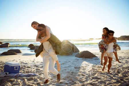 Téléchargez les photos : Deux hommes portant des femmes sur le dos à la plage au coucher du soleil. Photo de haute qualité - en image libre de droit