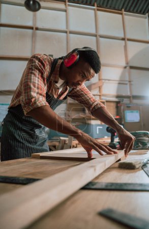 Foto de Hombre africano alinea pieza de madera mientras trabaja en proyecto de carpintería en almacén de carpintería. Foto de alta calidad - Imagen libre de derechos