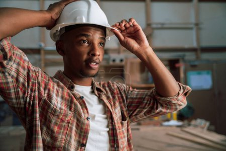 Photo for African American adjusts hardhat before working in carpentry factory . High quality photo - Royalty Free Image