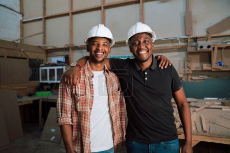 Foto de Los colegas afroamericanos que usan sombreros duros se colocan con los brazos entre sí en el almacén. Foto de alta calidad - Imagen libre de derechos
