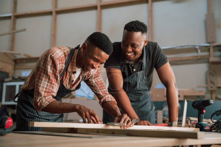 Foto de Un hombre afroamericano mide un trozo de madera, mientras que un colega africano ayuda en el taller de carpintería. Foto de alta calidad - Imagen libre de derechos