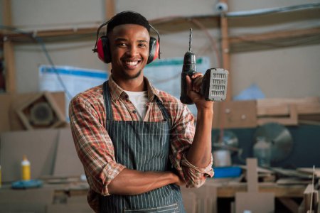 Foto de Sonriente hombre afroamericano posa con taladro eléctrico en taller de carpintería. Foto de alta calidad - Imagen libre de derechos