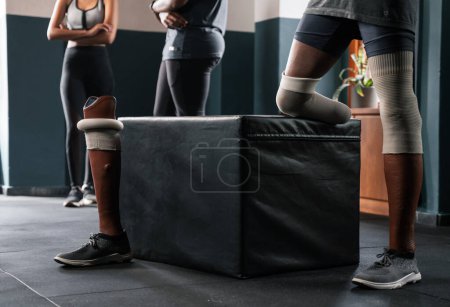 Téléchargez les photos : Trois personnes avec des jambes prothétiques sont debout ensemble dans une salle de gym. Leurs manches articulaires à la mode se fondent parfaitement avec leurs chaussures, car elles supportent leur poids sur le plancher - en image libre de droit