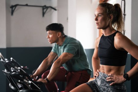 Foto de Un hombre y una mujer comparten una bicicleta estática en un edificio de gimnasio, trabajan los músculos de sus muslos y se divierten mientras están sentados en el equipo - Imagen libre de derechos