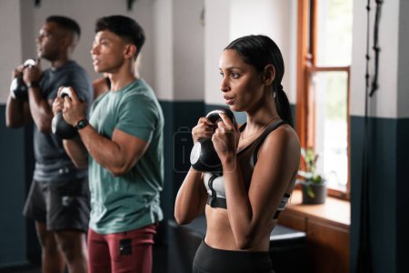 Photo for A group of people is performing kettlebell exercises in the gym, working on their arms, muscles, and thighs. There are also plants, windows, and doors in the room for added entertainment - Royalty Free Image