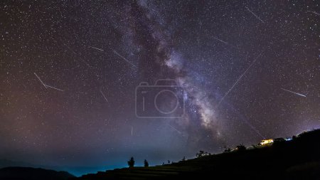 Langzeitbelichtung Nachtlandschaft mit der Milchstraße während Meteorschauer über einem Berg mit Hütte.