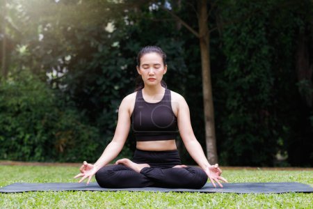 Asiatin praktiziert Yoga in Root Bond, Mula Bandha posiert auf der Matte im Outdoor-Park.