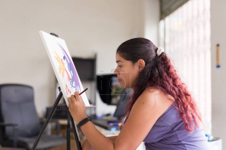 Téléchargez les photos : Femme adulte latine peignant à la maison le week-end. artiste passe-temps faire des œuvres d'art acrylique sur toile. détente et tranquillité - en image libre de droit