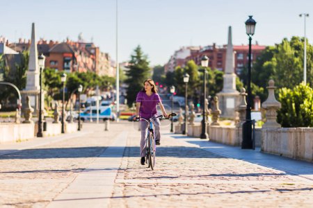 Photo for Middle aged adult woman biking in a city. cyclist eco friendly mobility for recreation and healthy leisure. copy space for spring or summer - Royalty Free Image