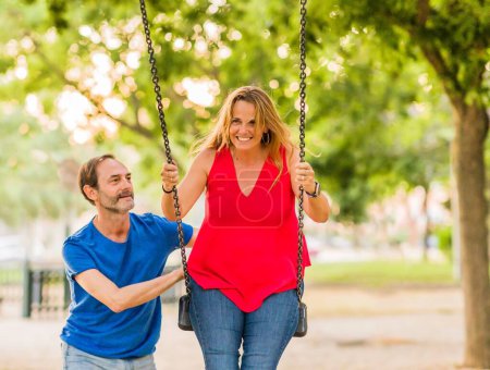 Téléchargez les photos : Hispanique senior homme et femme poussant balançant ensemble. style de vie relation avec sourire à l'extérieur. - en image libre de droit