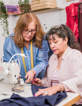 Photo for Mature Woman entrepreneur teaching how to use sewing-machine for eco-friendly reuse clothing for wardrobe. circular economy education together. - Royalty Free Image