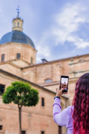 Téléchargez les photos : Lifestyle photo tenant téléphone portable à l'extérieur, en face d'un monument historique en Castille et Léon, Plaza de las Angustias à Salamanque, Espagne. Célèbre église catholique bâtiment religieux. ancien - en image libre de droit