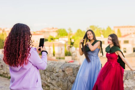 Photo for University campus young woman graduate, happy outdoors taking pictures with cellphone technology and log elegance dress. Spanish person with graduation stole - Royalty Free Image