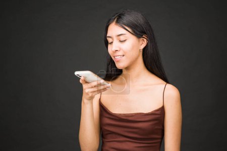 Photo for Hispanic young person, cheerful brunette portrait holding cellphone device. Isolated studio photo on black background - Royalty Free Image