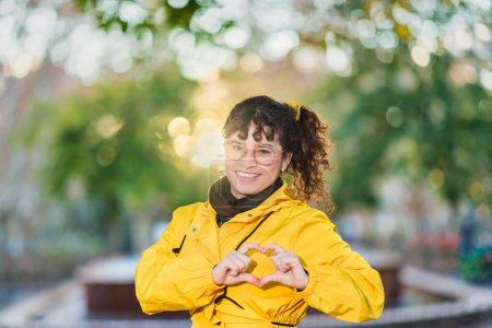 Photo for Hispanic Venezuelan mid-adult woman wearing a yellow raincoat outdoors portrait. march International Womens Day, iwd2023, doing zoomer gesture with hand - Royalty Free Image