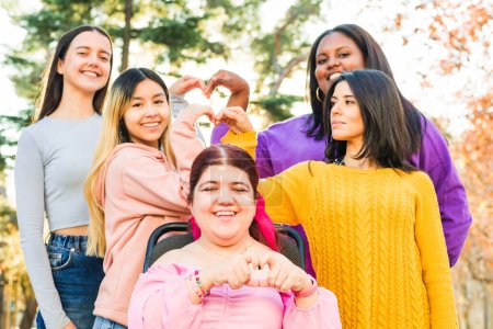 Téléchargez les photos : Les femmes amitié avec une personne en fauteuil roulant cause paralysie cérébrale. Multiculturelle heureux geste féministe pour l'inclusion, la coopération et la sororité - en image libre de droit