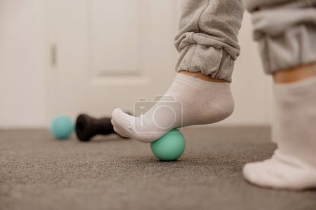 Woman doing flatfoot correction gymnastic exercise using massage ball. Myofascial relaxation of foot muscles. Hallux valgus. Pain. Identification of flat feet. Self care practices at home, healthcare