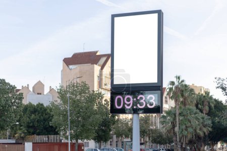Téléchargez les photos : Horloge numérique urbaine poste avec un panneau publicitaire vierge contre un paysage urbain, idéal pour les promotions. Modélisation verticale du panneau d'affichage, affichage vide. Espace de copie pour texte, image - en image libre de droit