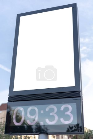 Téléchargez les photos : Horloge numérique urbaine poste avec un panneau publicitaire vierge contre un paysage urbain, idéal pour les promotions. Modélisation verticale du panneau d'affichage, affichage vide. Espace de copie pour texte, image - en image libre de droit