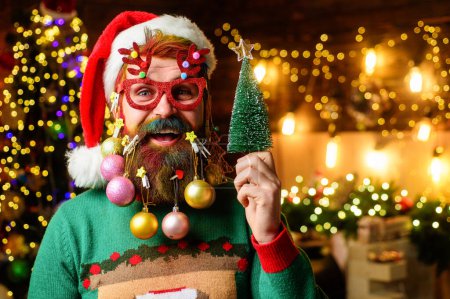 Téléchargez les photos : Homme barbu en chapeau de Père Noël et verres de fête avec petit arbre de Noël. Barbe décorée pour le Nouvel An - en image libre de droit
