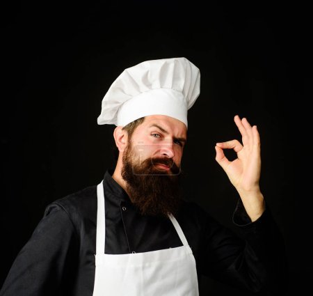 Chef in uniform and white apron showing sign ok, gesturing excellent. Cook with taste approval gesture. Bearded male chef with gesture for approving restaurant service. Chef with sign for delicious