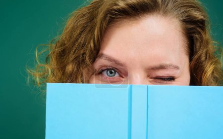 Photo for Close up portrait of winking teacher with notepad. School supplies. Back to school. Female college student hiding behind open book. Girl covers face with notebook. Knowledge day. Teacher in classroom - Royalty Free Image