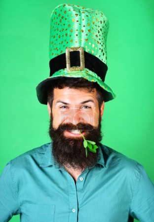 Photo for Patricks day celebration. Closeup portrait of bearded man in green top hat. Handsome man in leprechaun costume with clover in mouth. Smiling male with beard in leprechaun hat at Patricks day party - Royalty Free Image